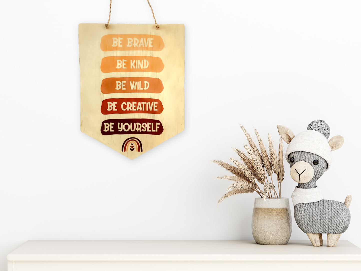 The "Be Brave, Be Kind, Be Creative, Be Wild, Be Yourself" wooden sign elegantly hung above a shelf. Below the sign, a charming ceramic sheep statue and dried foliage, enhancing the warm ambiance of the space.