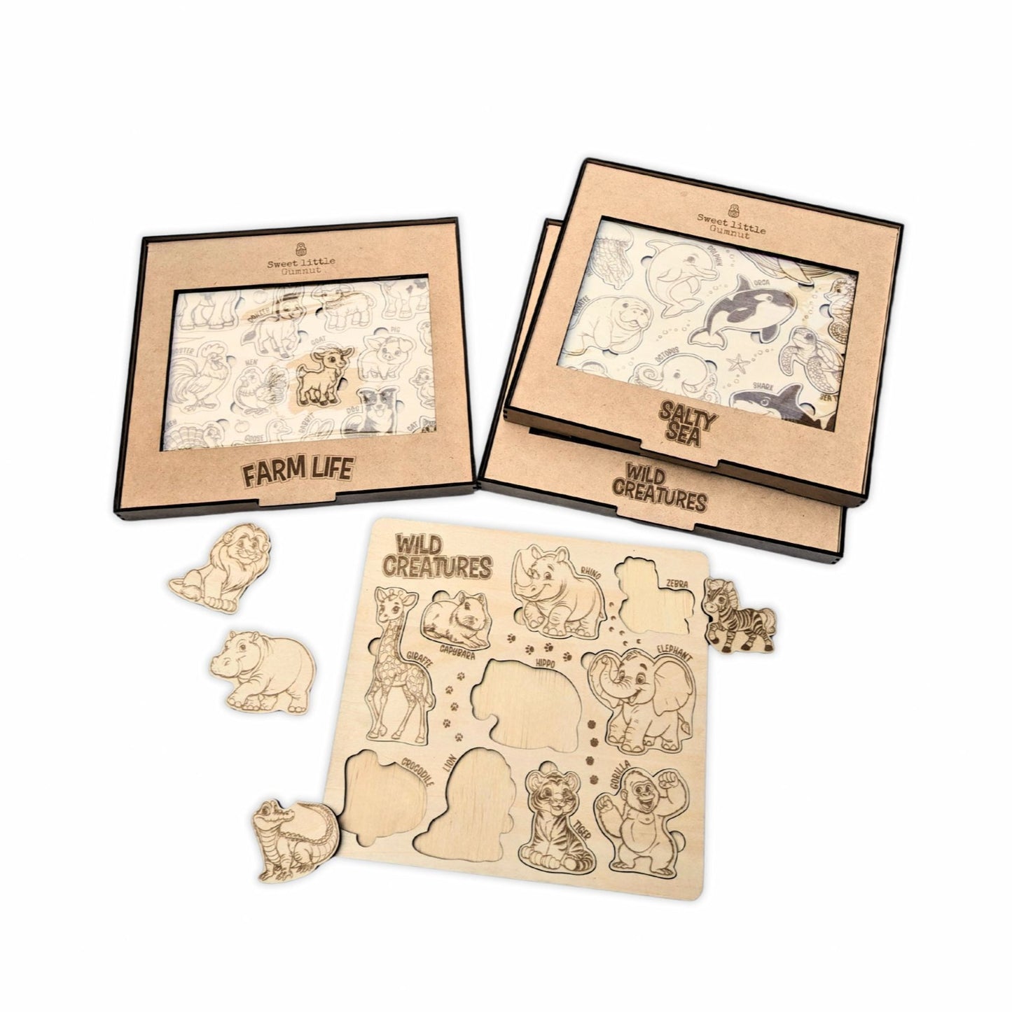 Photo of Three Animal Puzzles in Boxes - A photo showing three animal puzzles in boxes labeled "Farm Life," "Salty Sea," and "Wild Creatures." The "Wild Creatures" puzzle, featuring a lion, elephant, and gorilla, is displayed fully assembled in front of the boxes, highlighting the wooden, engraved animal designs.