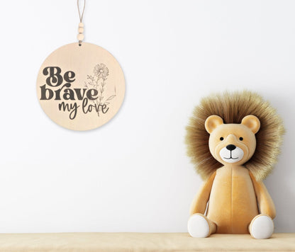 Wooden affirmation sign engraved with 'Be Brave, My Love,' positioned next to a plush toy lion, creating an inspiring and playful decor for a child's room.