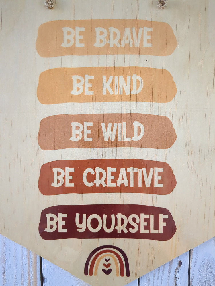 A detailed close-up of the "Be Brave, Be Kind, Be Creative, Be Wild, Be Yourself" wooden sign, highlighting the texture of the wood.