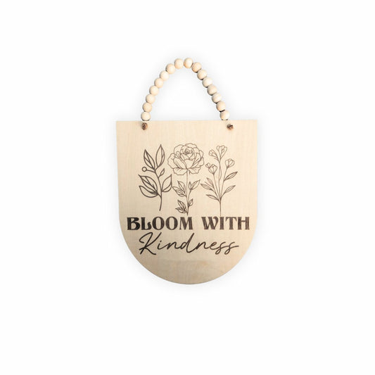 'Bloom with Kindness' Positive Affirmation Wooden Sign with an inverted arch shape, engraved flowers, and twine with wooden beads, displayed on a plain background.