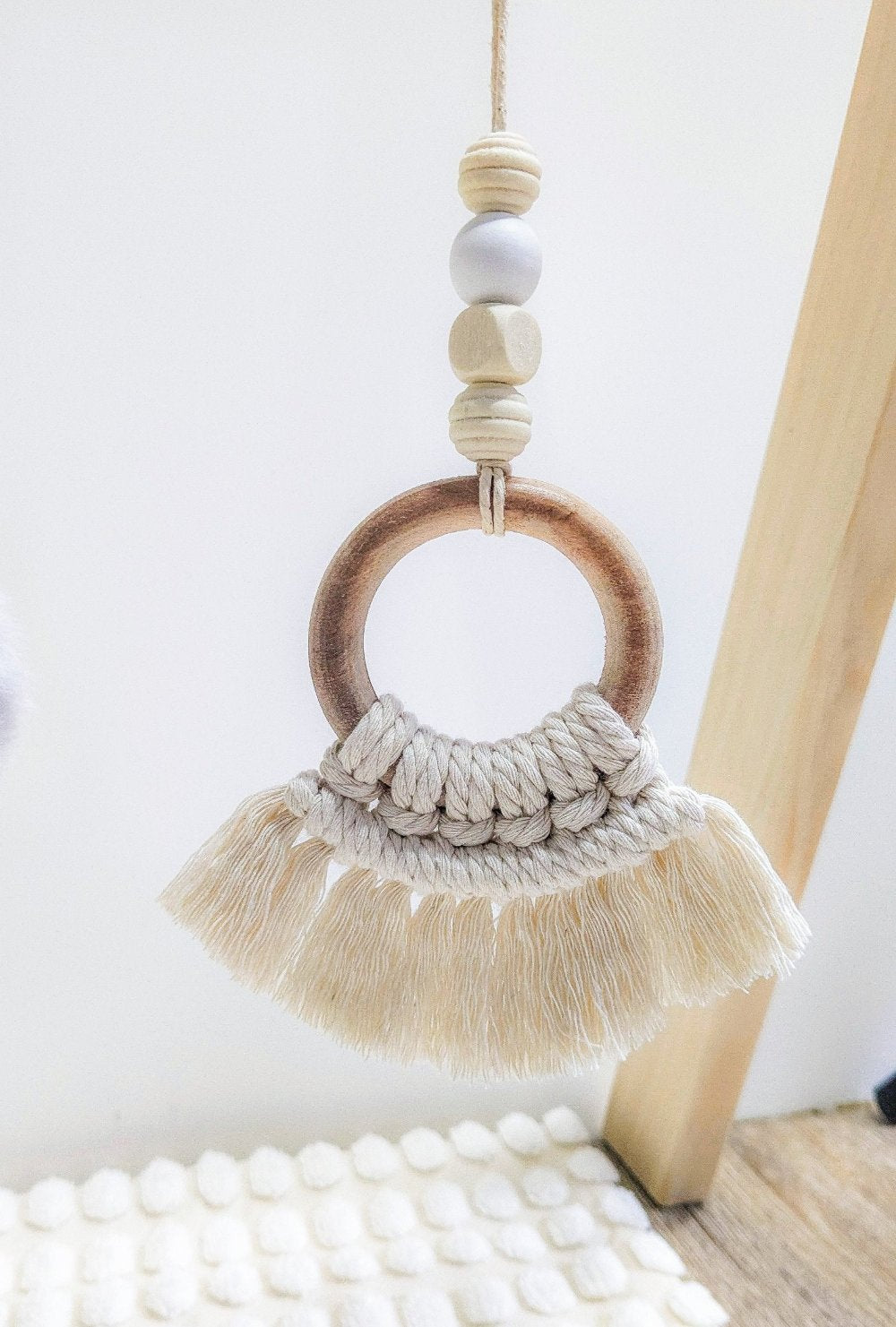 The large wooden circle with macrame tassels hanging from the baby gym, displaying its beautiful design and wooden beads.