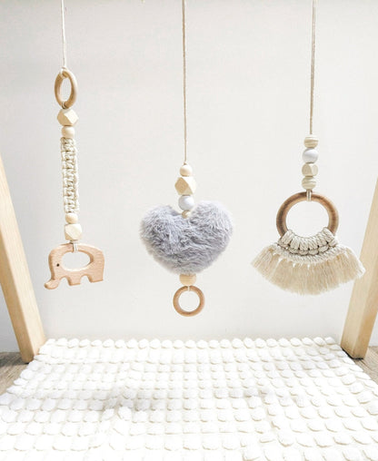 The three Boho macrame play gym toys hanging from a wooden baby gym, showcasing their unique designs and textures.