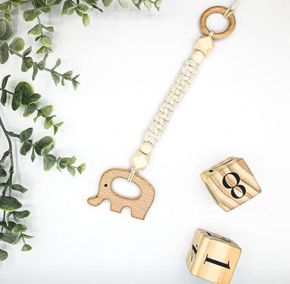 A wooden elephant macrame play gym toy positioned alongside green leaves and wooden number squares, showcasing its unique design and the natural elements around it.