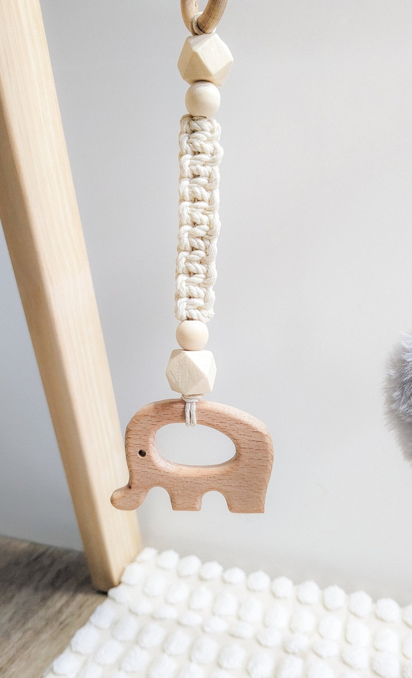  The wooden elephant macrame toy suspended from the baby gym, featuring intricate details and wooden beads.